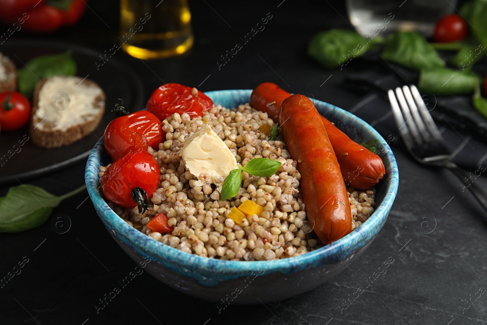 Photo of Tasty buckwheat porridge with sausages on black table