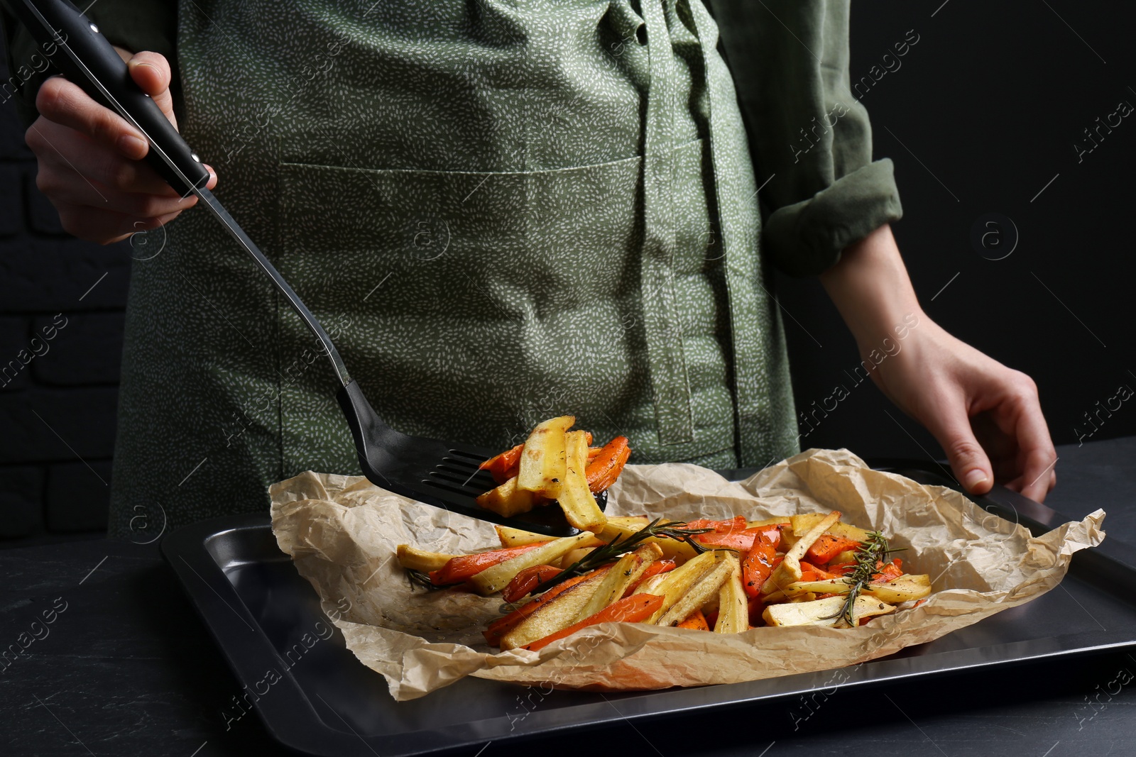 Photo of Cooker near baking pan with tasty parsnip and bell pepper at dark grey table, closeup