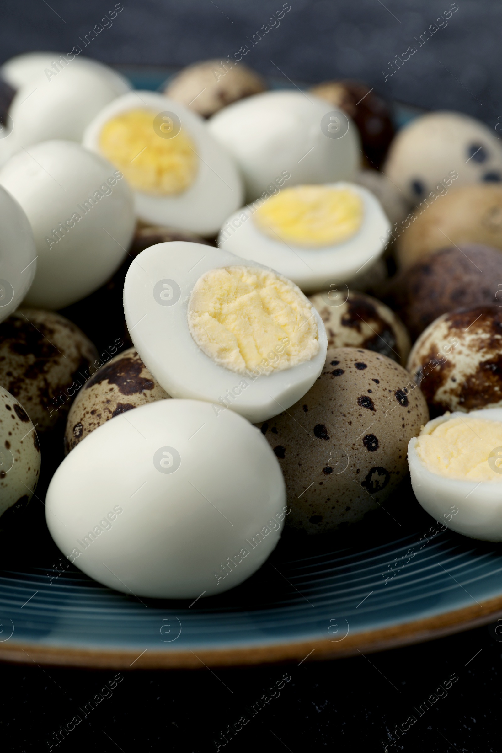 Photo of Peeled and unpeeled hard boiled quail eggs in plate on black table, closeup