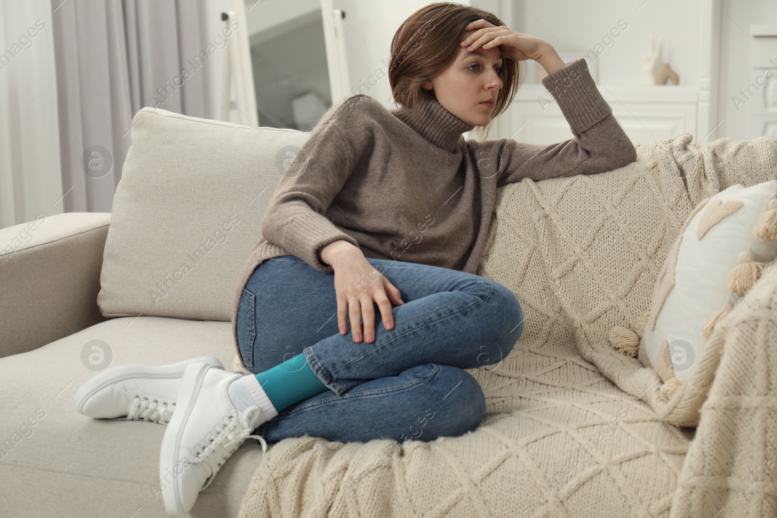 Photo of Sad young woman sitting on sofa at home