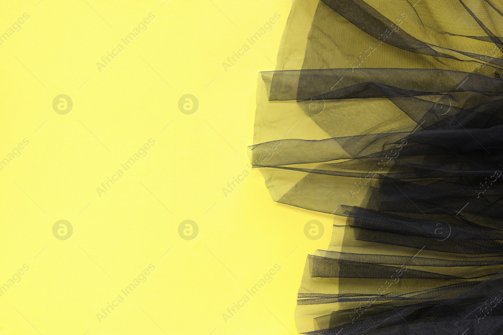 Photo of Beautiful black tulle fabric on yellow background, top view. Space for text
