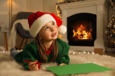 Cute child writing letter to Santa Claus while lying on floor at home. Christmas celebration