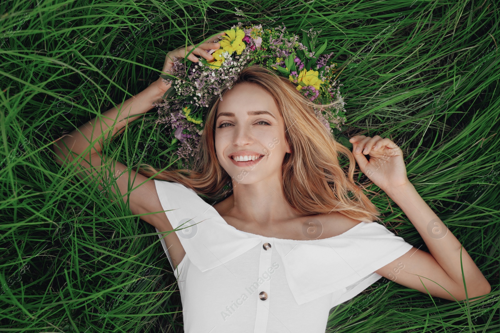 Photo of Young woman wearing wreath made of beautiful flowers on green grass, top view