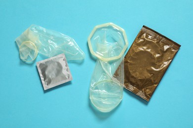 Photo of Unrolled female, male condoms and packages on light blue background, flat lay. Safe sex