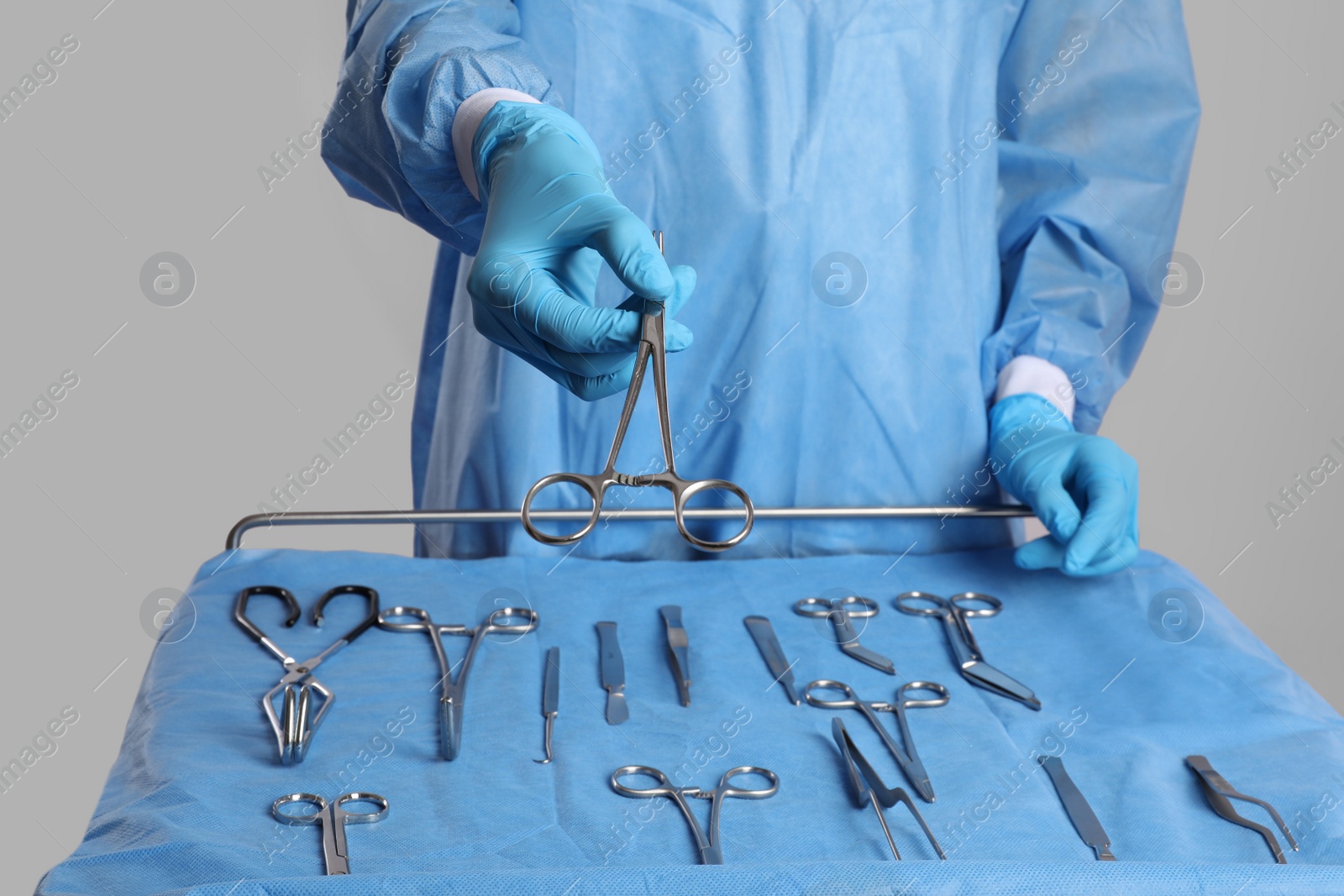 Photo of Doctor giving scissors near table with different surgical instruments on light background, closeup