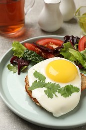 Photo of Plate with tasty fried egg, slice of bread and salad on light grey table, closeup