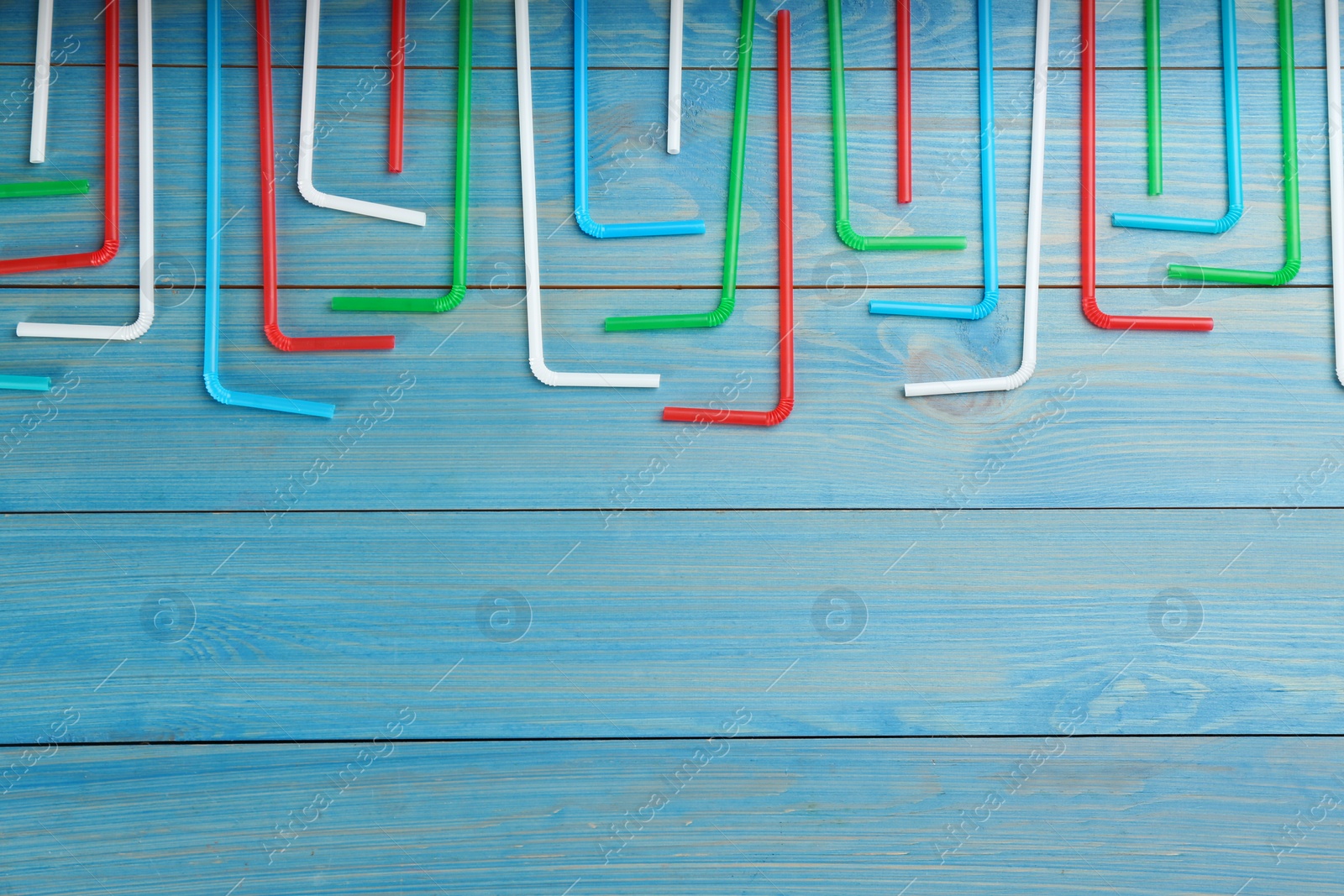 Photo of Colorful plastic drinking straws on light blue wooden table, flat lay. Space for text