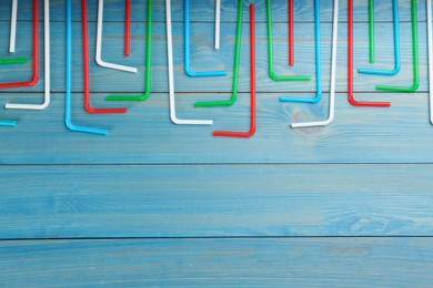 Colorful plastic drinking straws on light blue wooden table, flat lay. Space for text