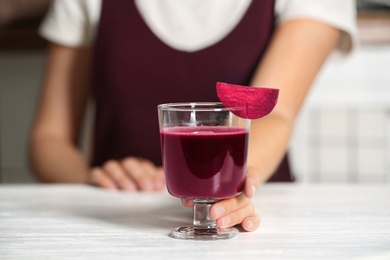 Photo of Woman with glass of beet smoothie at table, closeup