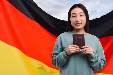 Immigration. Woman with passport and national flag of Germany against blue sky, space for text