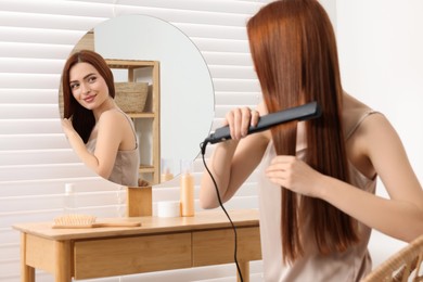 Photo of Beautiful woman using hair iron near mirror in room