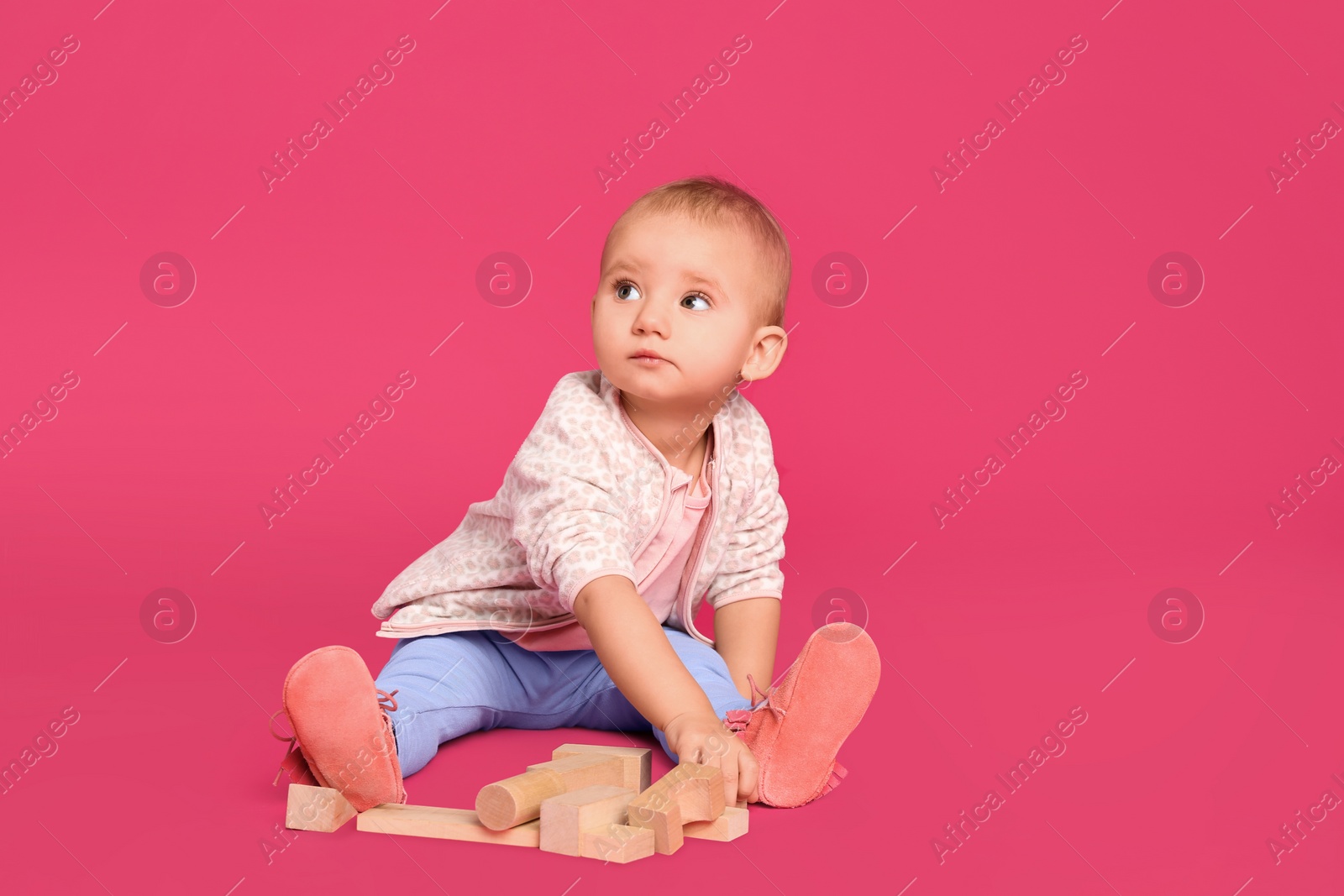 Photo of Cute child playing with wooden building blocks on pink background