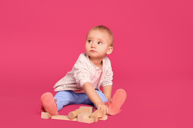 Cute child playing with wooden building blocks on pink background