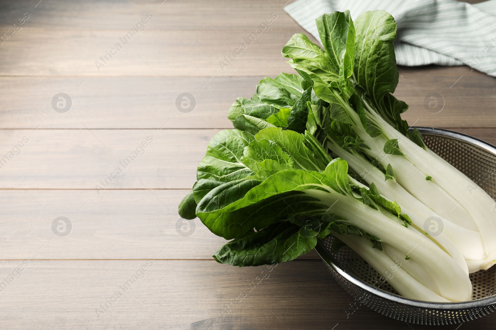 Photo of Fresh green pak choy cabbages in colander on wooden table, space for text