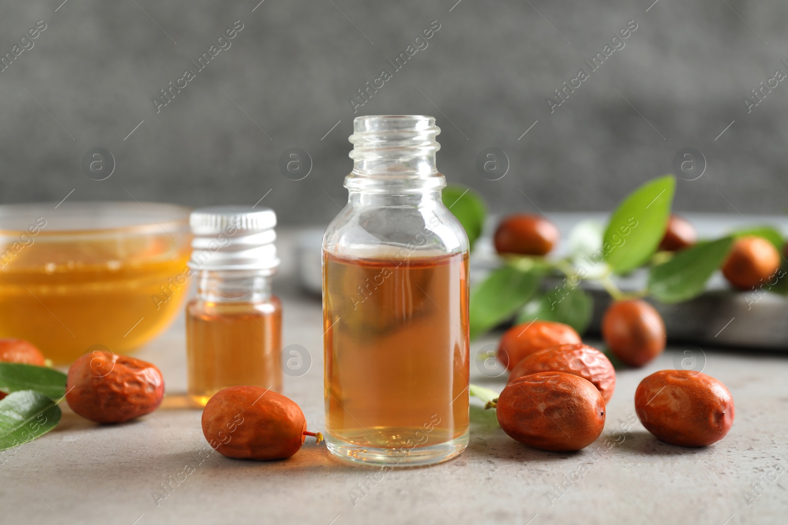 Photo of Glass bottle with jojoba oil and seeds on grey stone table