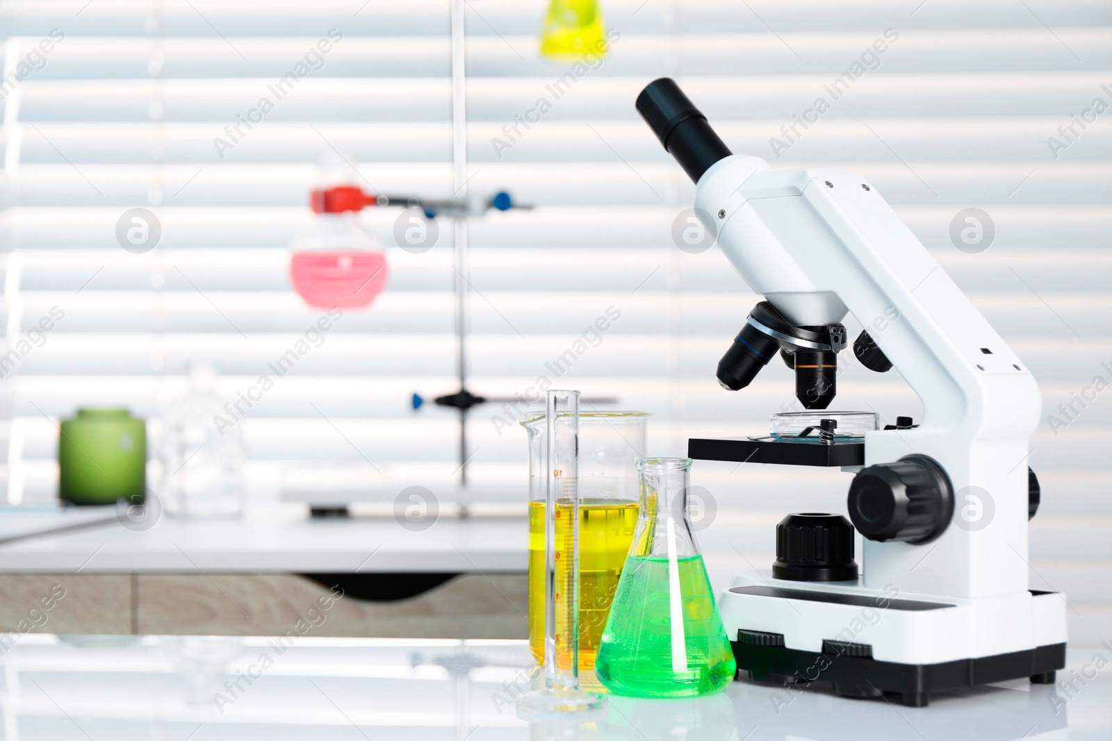 Photo of Laboratory analysis. Different glassware with liquids and microscope on white table indoors