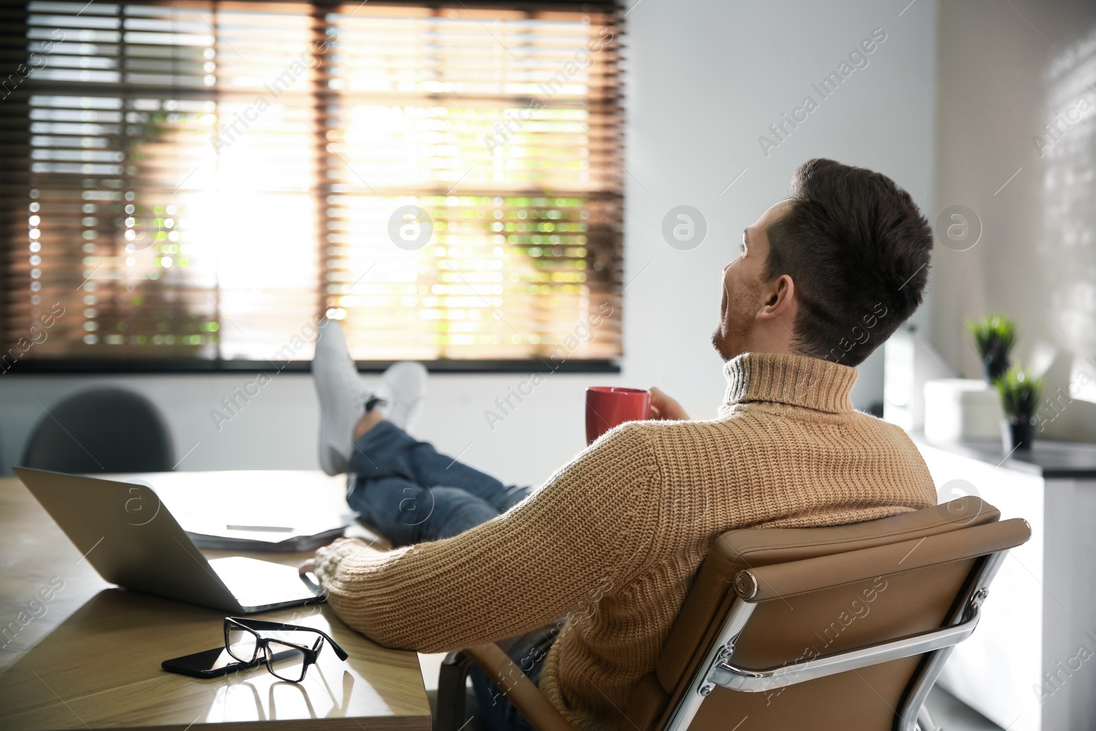 Photo of Young man with cup of drink relaxing at workplace