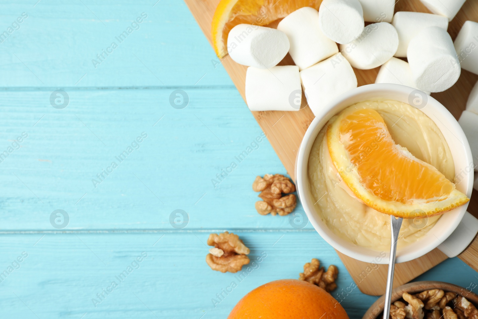 Photo of Dipping slice of orange into pot with white chocolate fondue on blue wooden table, top view. Space for text