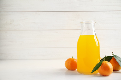 Photo of Fresh tangerines and bottle of juice on white wooden table. Space for text