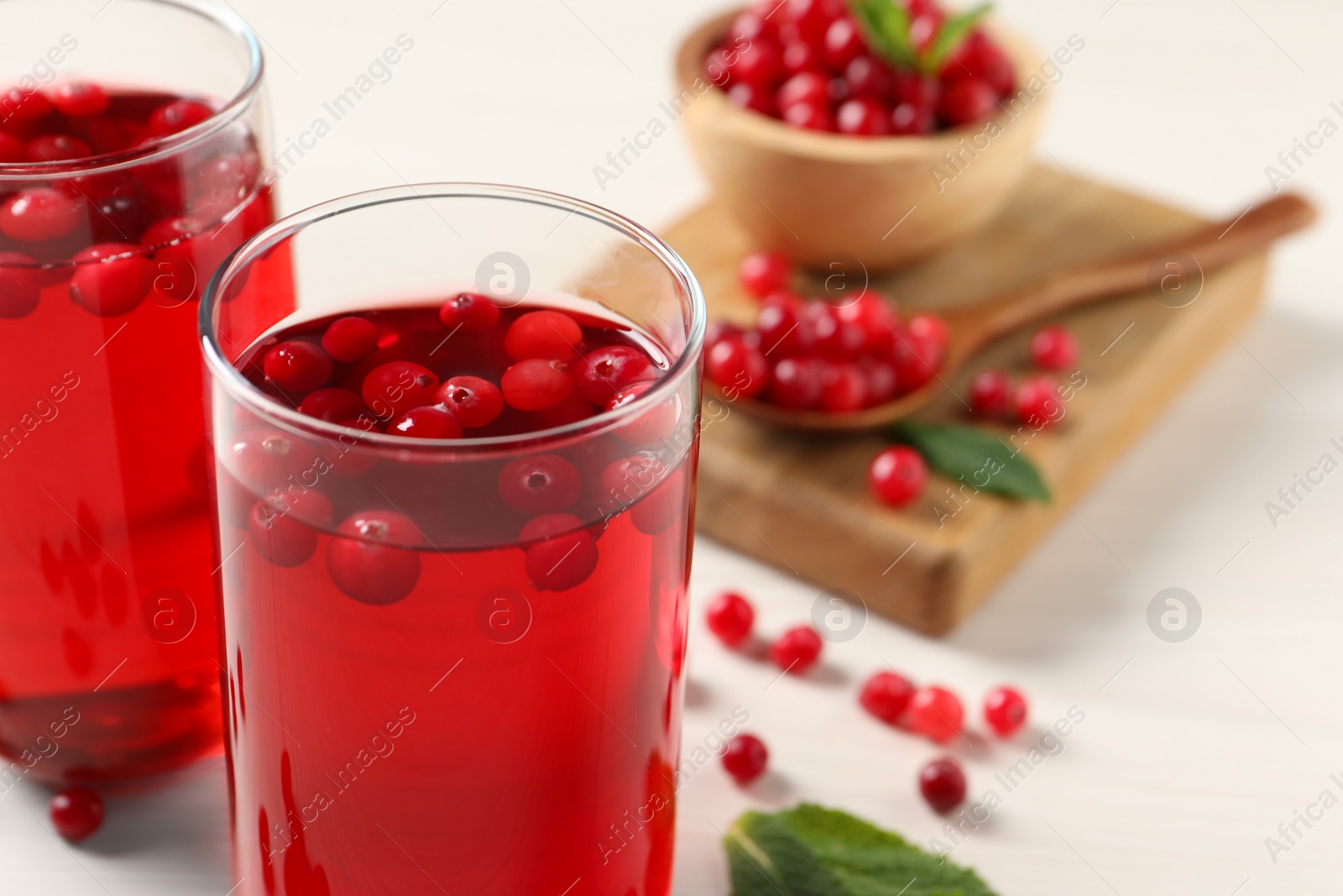 Photo of Tasty cranberry juice in glasses and fresh berries on white wooden table, closeup. Space for text