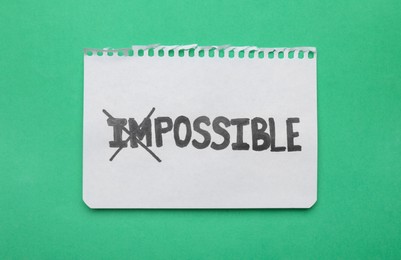 Photo of Motivation concept. Paper with changed word from Impossible into Possible by crossing over letters I and M on green background, top view