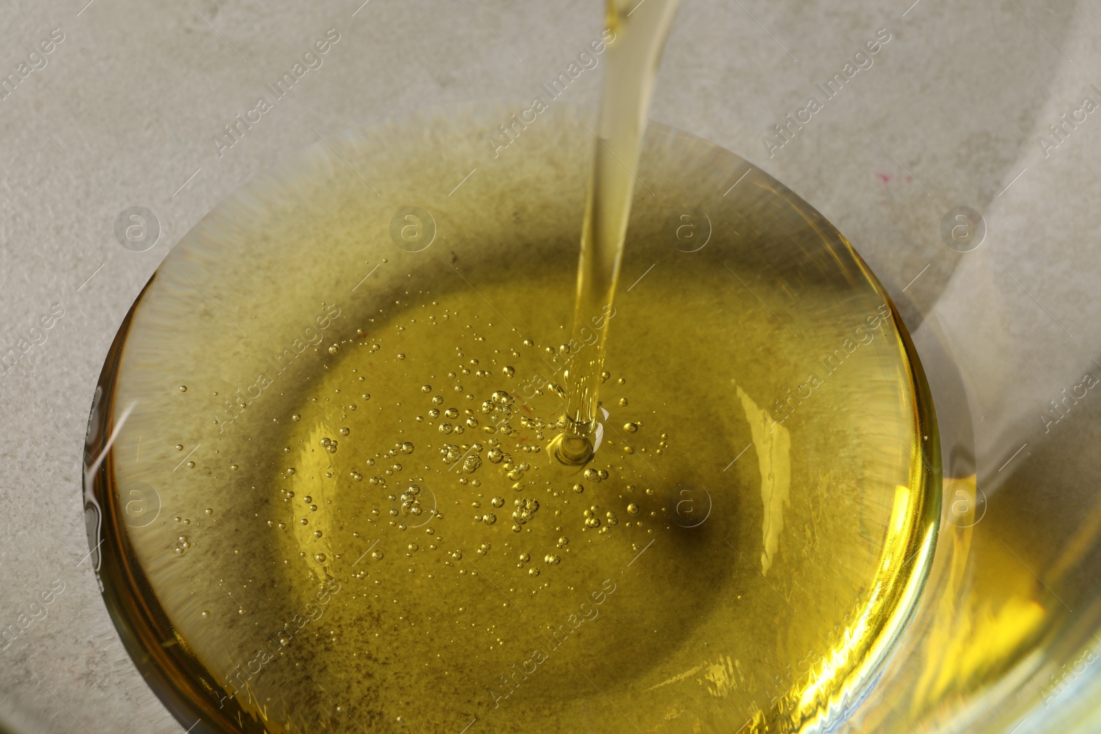 Photo of Pouring cooking oil into glass bowl, closeup