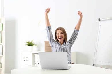 Emotional young woman with laptop celebrating victory in office