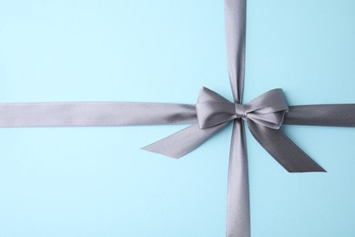 Photo of Grey satin ribbon with bow on light blue background, top view