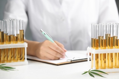 Photo of Test tubes with urine samples, hemp leaves and blurred doctor on background