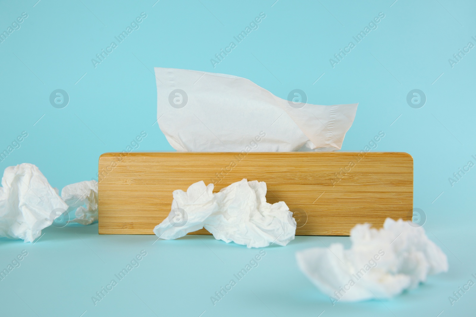 Photo of Used paper tissues and wooden holder on light blue background