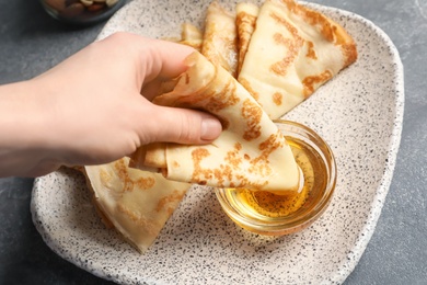 Photo of Woman dipping thin pancake into bowl with honey, closeup