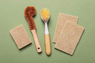 Photo of Cleaning brushes and sponges on green background, flat lay