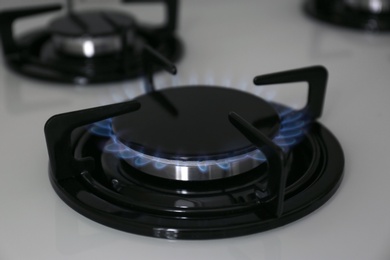 Gas burner with blue flame on modern stove, closeup