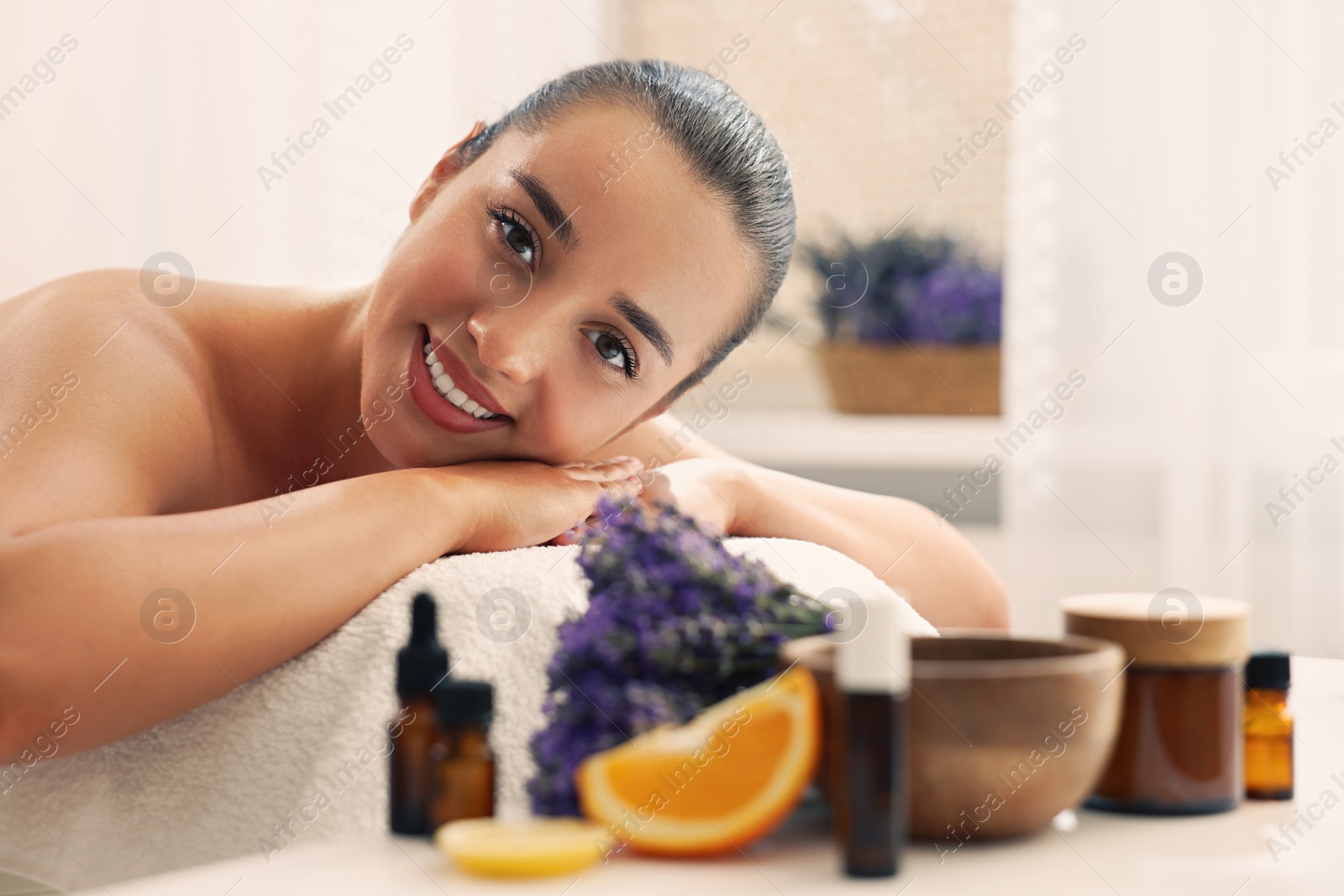 Photo of Beautiful young woman relaxing on massage couch and bottles of essential oil with ingredients on table in spa salon