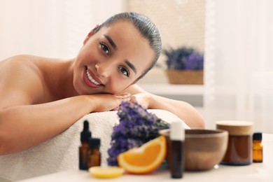 Beautiful young woman relaxing on massage couch and bottles of essential oil with ingredients on table in spa salon