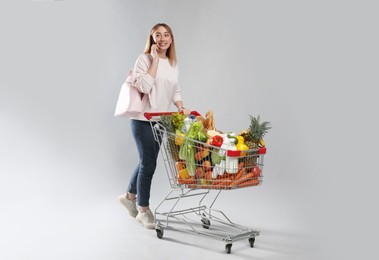 Photo of Young woman with shopping cart full of groceries talking on phone against grey background