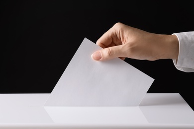 Photo of Woman putting her vote into ballot box on black background, closeup
