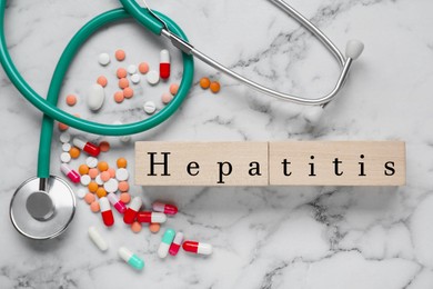 Word Hepatitis made of wooden cubes, stethoscope and pills on white marble table, flat lay