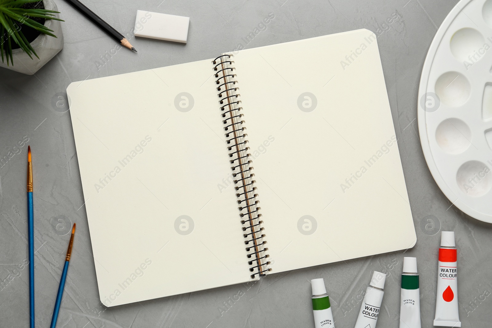 Photo of Flat lay composition with blank sketchbook on light grey stone table. Space for text