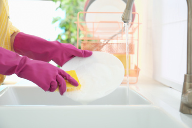 Woman washing ceramic plate in kitchen, closeup