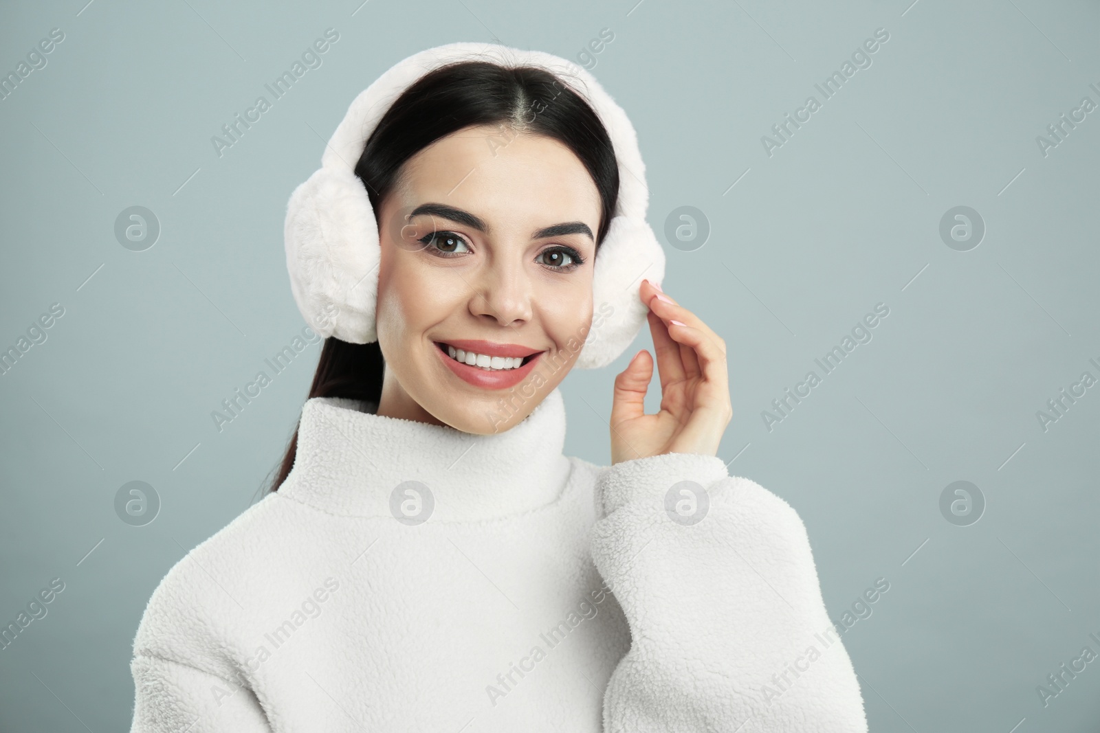 Photo of Beautiful young woman wearing earmuffs on light grey background