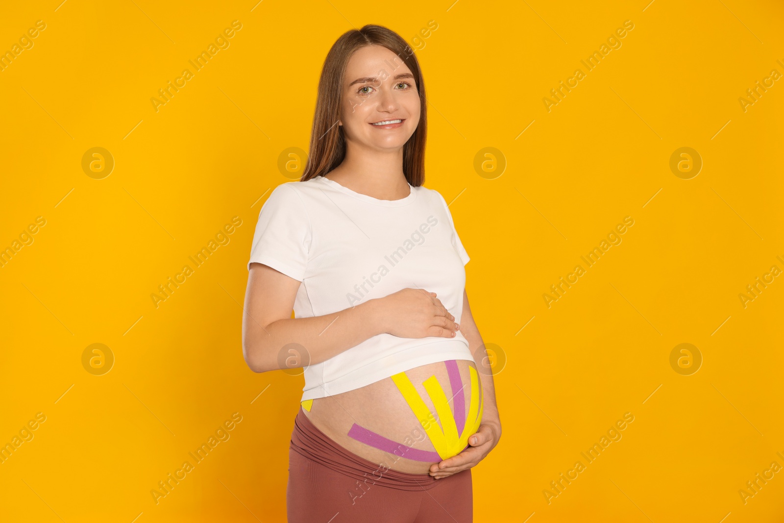 Photo of Pregnant woman with kinesio tapes on her belly against orange background