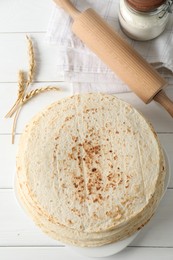 Tasty homemade tortillas, flour, spikes and rolling pin on white wooden table, top view