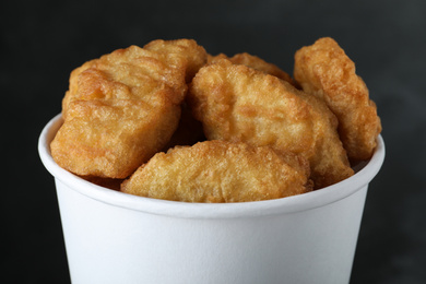 Photo of Bucket with delicious chicken nuggets on grey background, closeup