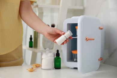 Photo of Woman taking cosmetic product out of mini refrigerator indoors, closeup