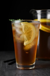 Photo of Delicious iced tea on grey table against black background, closeup