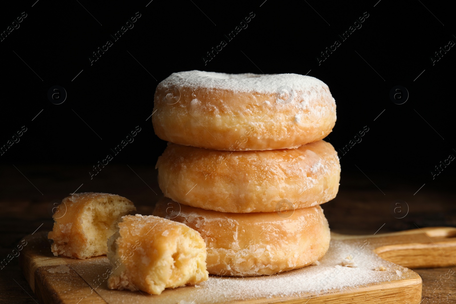 Photo of Delicious donuts with powdered sugar on wooden table