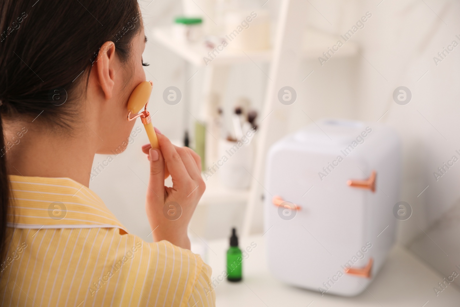 Photo of Woman doing face massage at dressing table with cosmetic refrigerator indoors