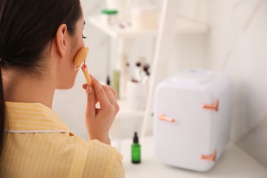 Photo of Woman doing face massage at dressing table with cosmetic refrigerator indoors