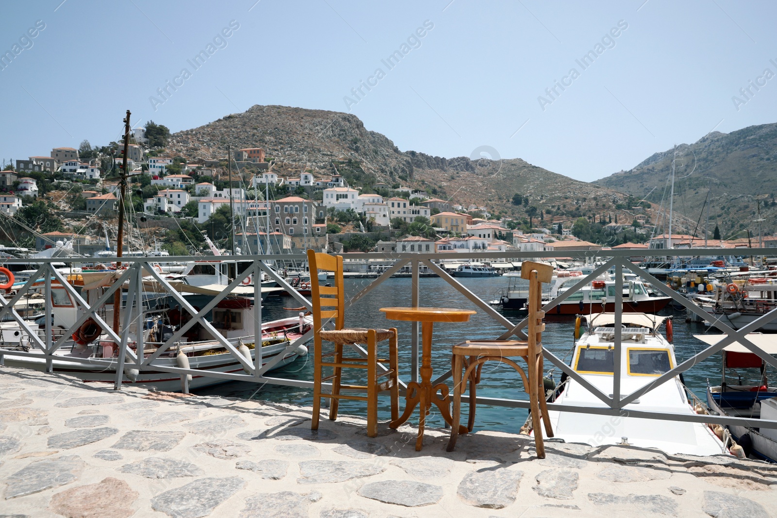 Photo of Wooden table and chairs near port with different boats on sunny day